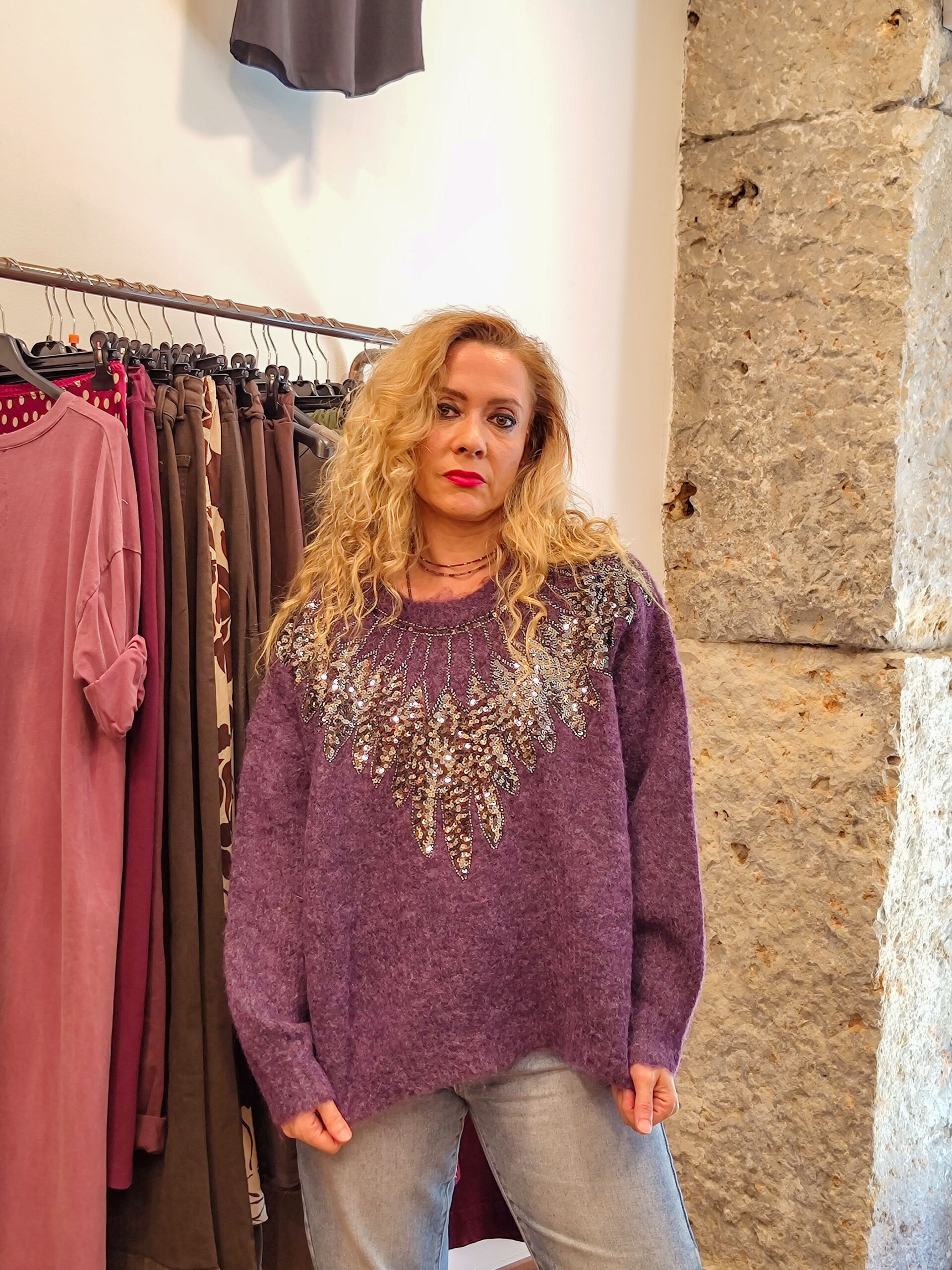 Mujer con jersey morado oversize con lentejuelas en los hombros y escote, combinado con vaqueros claros.